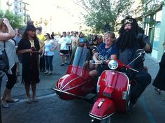 two people on a motor scooter with long black hair and beards in costume