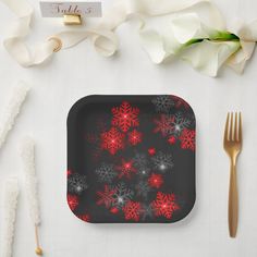 a black plate with red snowflakes on it next to silverware and flowers