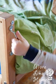 a child's hand holding onto a wooden bed frame