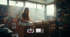 a woman standing behind a box filled with records in a room full of record players