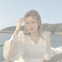 a woman in a white dress is posing for a photo by the water with her hand on her head