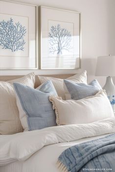 two framed pictures hang above a bed with white linens and blue pillows on it