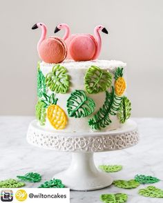 two flamingos sitting on top of a cake with pineapples and palm leaves