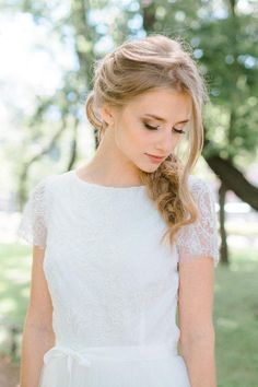 a woman wearing a white dress and braid in her hair is looking down at the ground