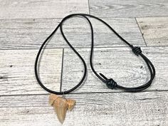 a necklace with an arrow shaped pendant hanging from it's side on a wooden floor