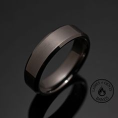 a wedding band with a brushed finish is shown on a black surface, and has a flame symbol in the center