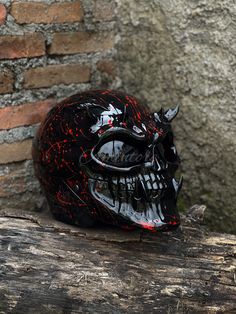 a black helmet with red paint splattered on it sitting on a piece of wood