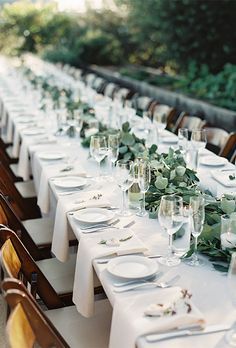 a long table is set with white plates and silverware