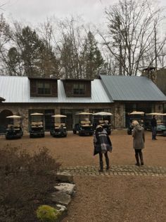 two people standing in front of a building with several golf carts parked on the driveway