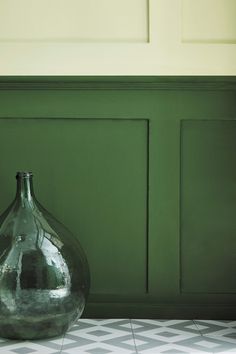 a glass vase sitting on top of a tiled floor next to a green painted wall