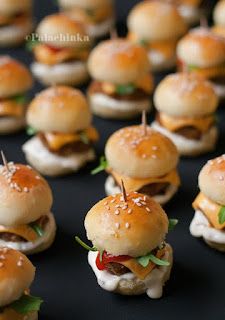 mini burgers with toothpicks in them on a black tableclothed surface