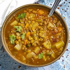 a bowl filled with soup and vegetables on top of a blue table cloth next to a spoon