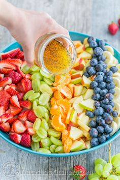 a person pouring dressing into a bowl of fruit on a table with strawberries and grapes