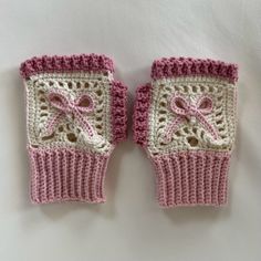 two pink and white crocheted mittens with bows on them sitting next to each other