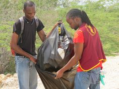 two men standing next to each other holding trash bags and looking at something in the bag