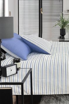 a bed with blue and white striped sheets, pillows and a clock on the nightstand