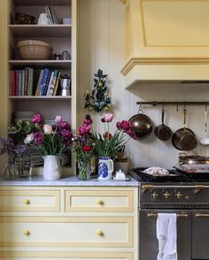 a kitchen with pots and pans on the stove next to flowers in vases