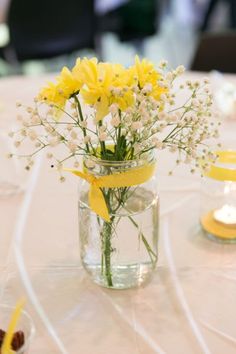 yellow flowers are in a mason jar on a white tablecloth with candles and other decorations