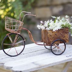 an old fashioned bicycle with flowers in the basket is sitting on a wooden table outside