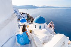 a woman in a blue dress sitting on the edge of a building looking at the ocean