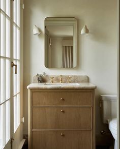 a white toilet sitting next to a bathroom sink under a mirror on top of a wooden cabinet