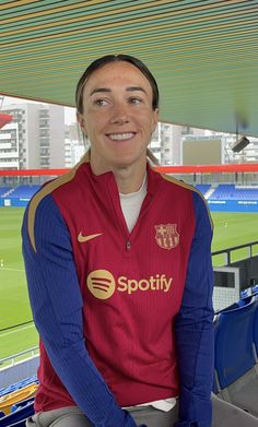 a woman is sitting in the stands at a soccer game wearing a red and blue jacket