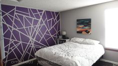 a white bed sitting in a bedroom next to a purple and white wall with geometric designs on it