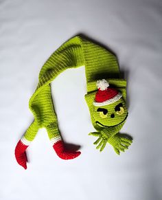 a knitted green frog laying on top of a white sheet wearing a red and white hat