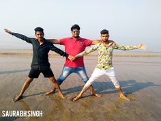 three men are standing on the beach posing for a photo with their arms spread out