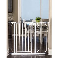 a white baby gate in front of a dining room table with chairs and a potted plant