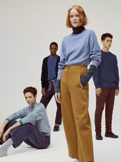 a group of people standing and sitting in front of a white background, all wearing sweaters