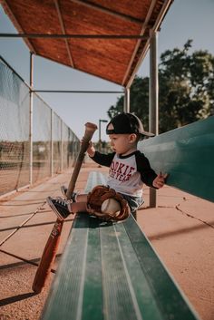 a little boy sitting on top of a bench holding a baseball bat and ball in his hand