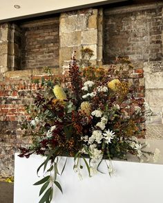 a bouquet of flowers sitting on top of a white box in front of a brick wall