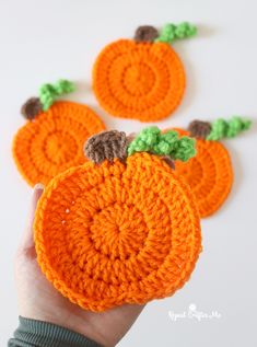 crocheted pumpkins with leaves on them are being held up by someone's hand