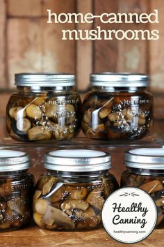 six jars filled with pickles sitting on top of a wooden table next to a sign that says, home - canned mushrooms