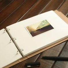 an open notebook on a wooden table next to a pen