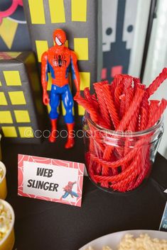 there is a spider man party table with candy sticks in the bowl and other decorations