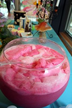 a glass filled with pink liquid on top of a blue table next to a window