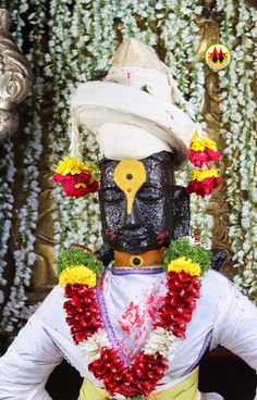 a man dressed in costume standing next to a wall with flowers on it's head