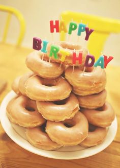 a stack of doughnuts on a plate with happy birthday candles in the middle