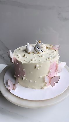 a cake with white frosting and pink butterflies on it, sitting on a plate