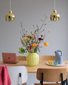 a vase with flowers sitting on top of a wooden table next to a laptop computer