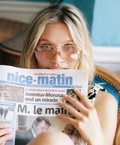 a woman sitting in a chair holding up a newspaper to her face and looking at the camera