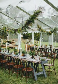 an outdoor tent set up with tables and chairs, greenery hanging from the ceiling