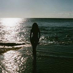 a woman is standing in the water at the beach with her back to the camera