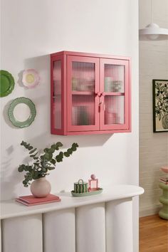 a pink cabinet sitting on top of a white wall next to a potted plant