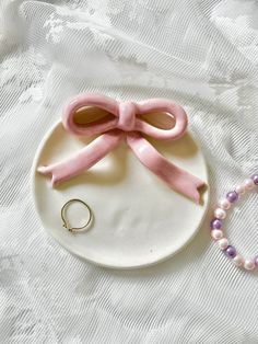 a white plate topped with a pink bow next to a ring on a beaded necklace