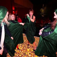 four women dressed in green cloths are dancing on the floor with leaves all around them