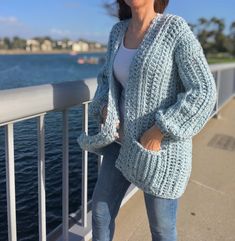 a woman standing on a bridge next to the water wearing a blue knitted cardigan