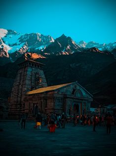 a group of people standing around a building with mountains in the background